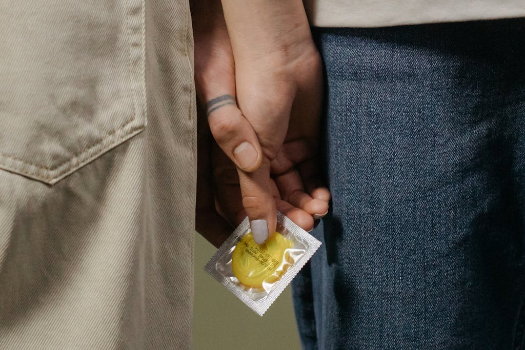 Close-up image of a couple holding hands with a condom, symbolizing safe sex.