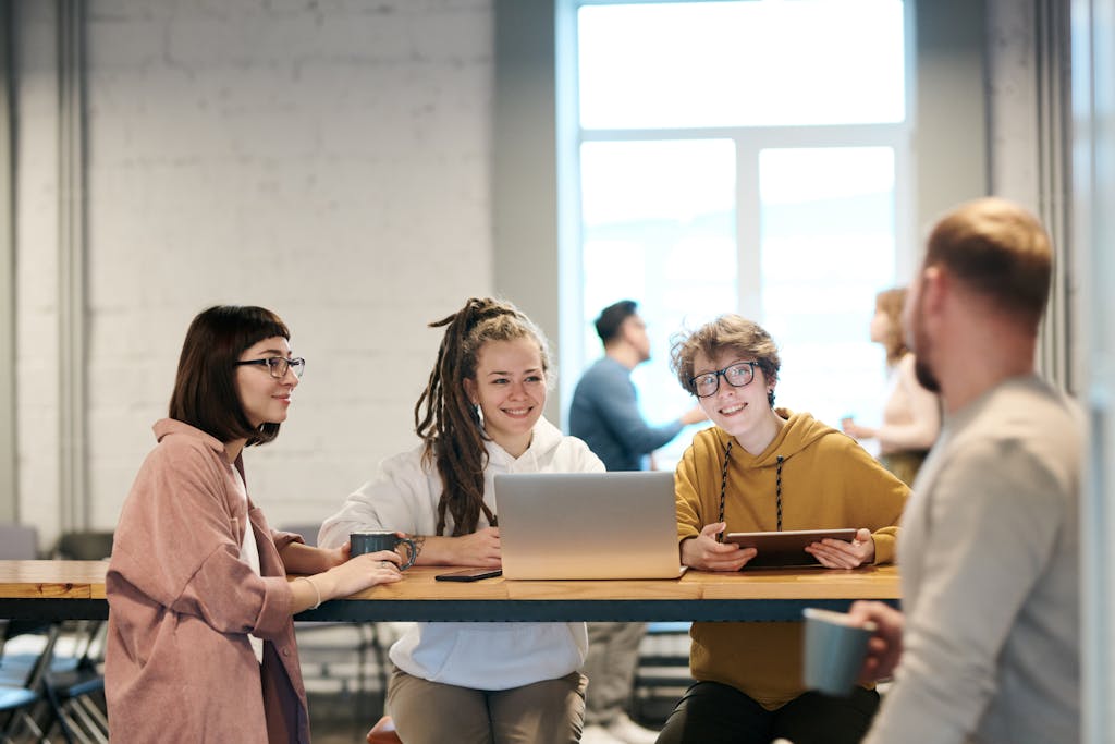 A diverse group of young professionals brainstorming in a modern office setting, discussing ideas with laptops and tablets.