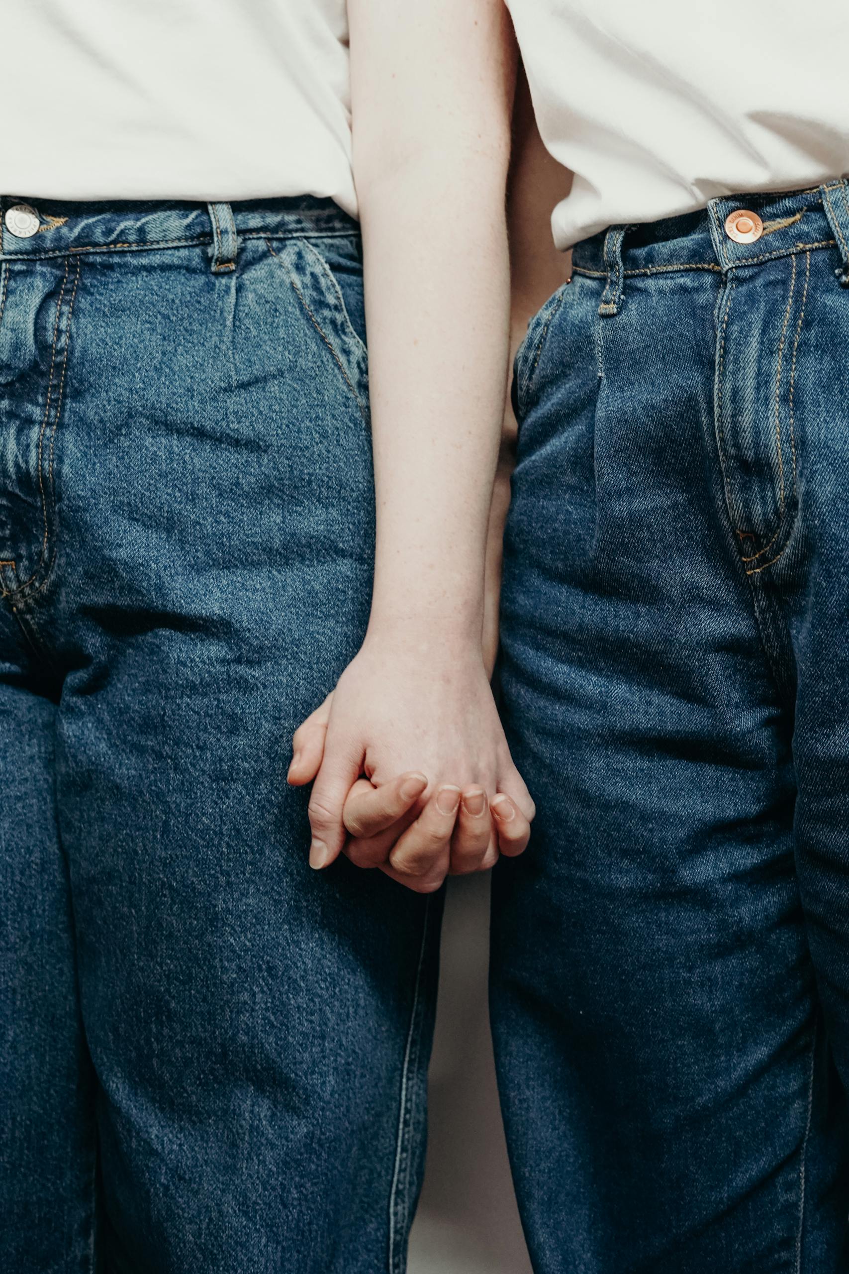 Intimate close-up of a couple in denim jeans holding hands, symbolizing love and connection.